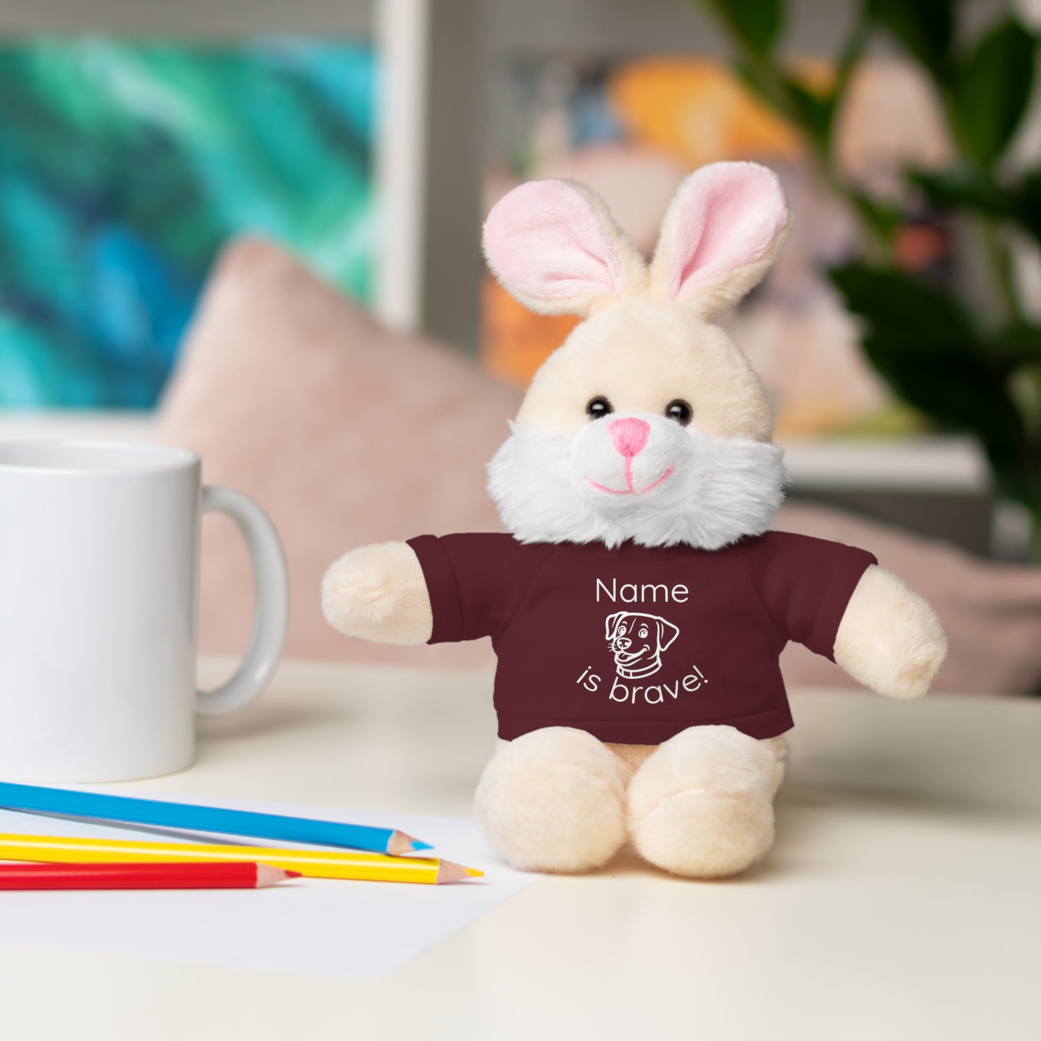 Soft off white plush bunny wearing a Name is Brave personalized maroon  tee shirt - sitting on desk with colored pencils