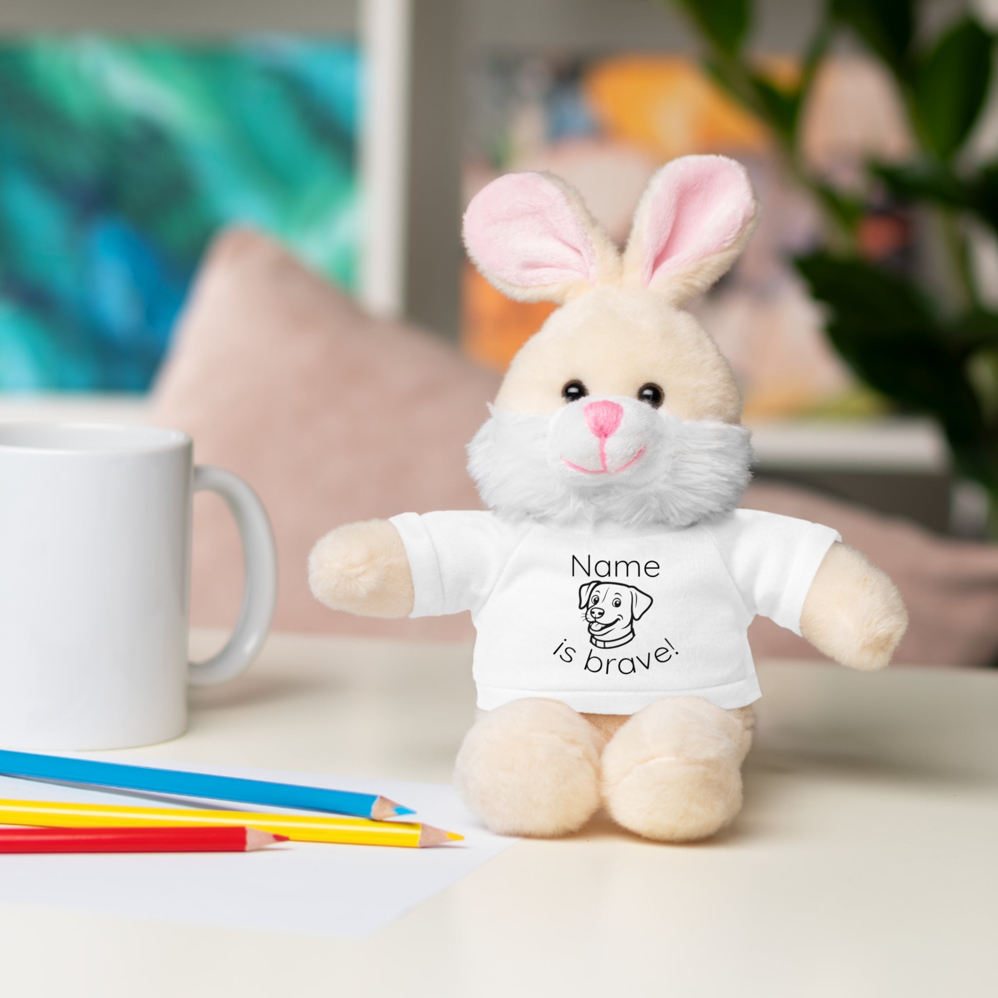 Soft off white plush bunny wearing a Name is Brave personalized white  tee shirt - sitting on desk with colored pencils